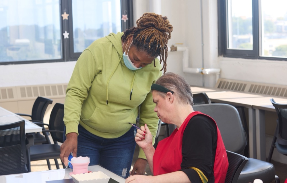 A NeuSpark staff member helping a program participant with an activity at a classroom table