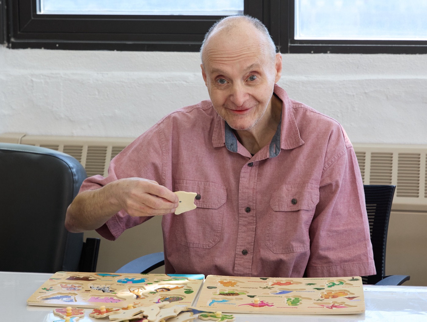 A program participant smiling while working on wooden puzzles